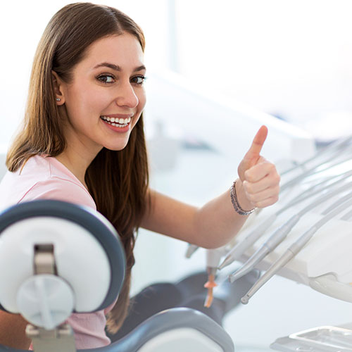 Beautiful woman sitting in a dental bed smiling with thumbs up