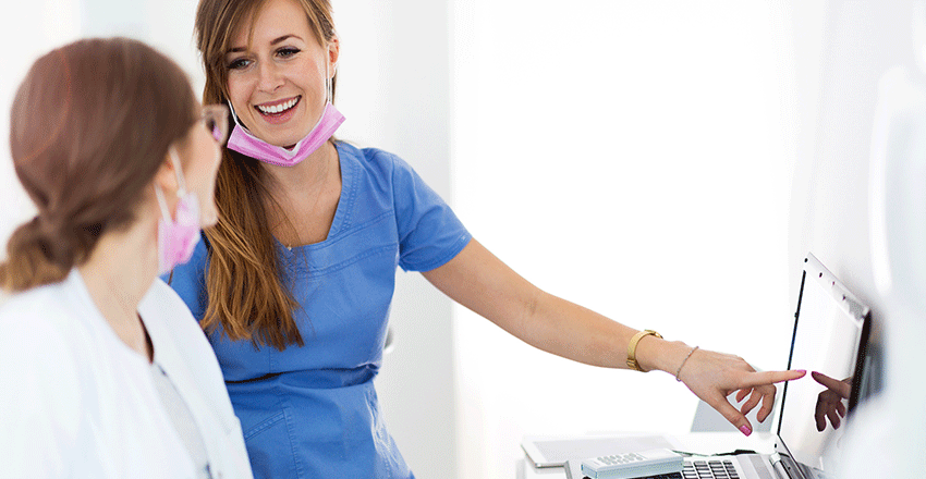 Dentist talking to her dental assistant who is pointing its finger in a dental monitor