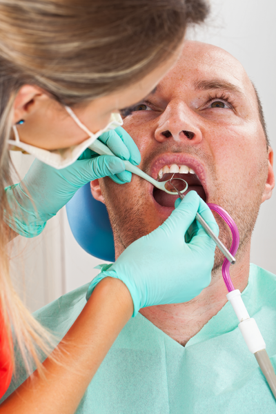 A dentist wearing gloves and a mask examines a male patient's open mouth using dental instruments during a checkup to assess oral health and screen for gum disease. peridoontal